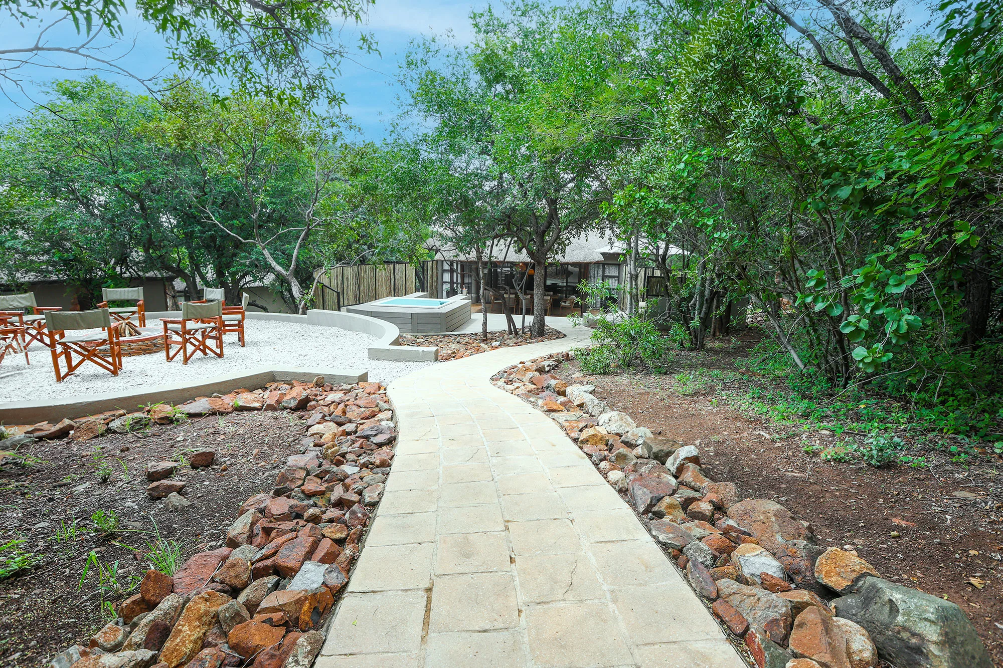 A paved lodge pathway leading past a fire pit and plunge pool to thatched suites