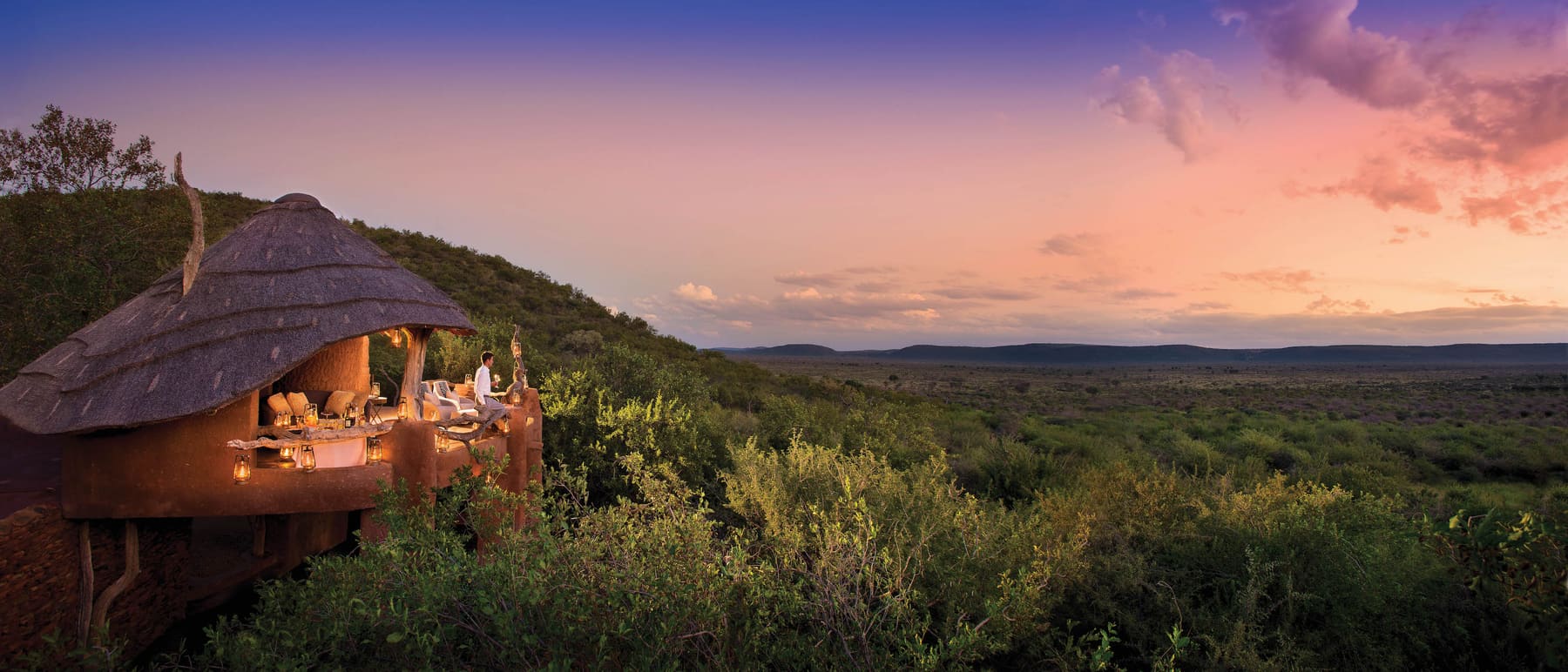 A thatched lookout deck lit by lanterns above the Madikwe bushveld at sunset