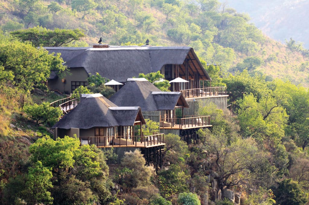 Thatched lodge chalets on stilts stepping down a green hillside above the valley