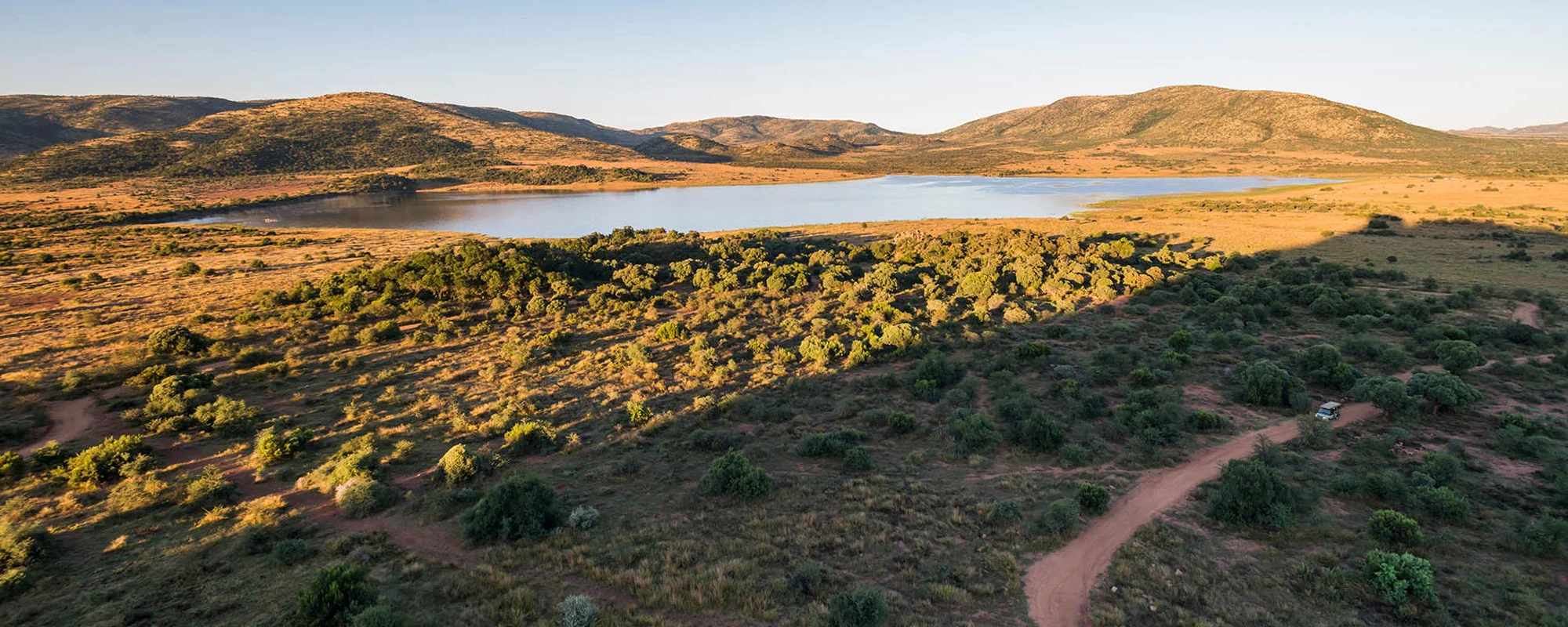 Aerial view of Pilanesberg grassland, a dam and volcanic hills in low golden light