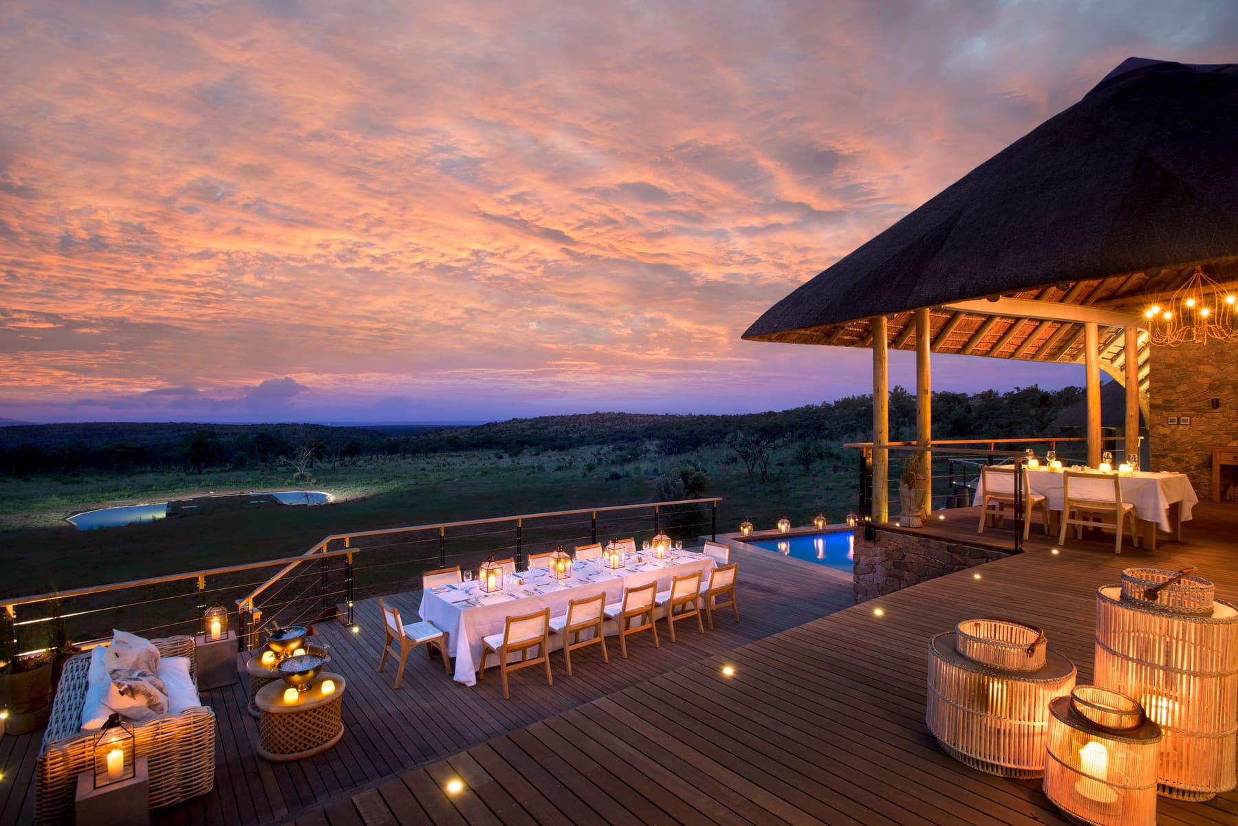 A candlelit dining table on a lodge deck under a pink Waterberg sunset